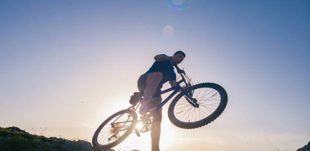 istock Strong fit male mountain biker performing stunts on rocky terrain on a sunset while wearing a blue shirt and riding a blue bike 1364685363