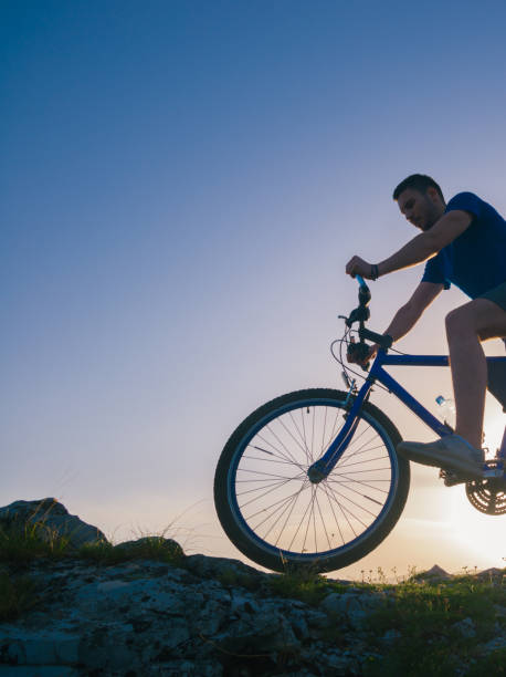 istock Strong fit male mountain biker performing stunts on rocky terrain on a sunset while wearing a blue shirt and riding a blue bike 1364685366