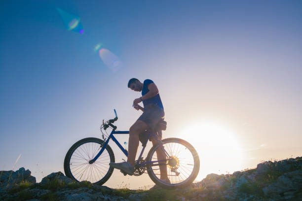 istock Strong fit male mountain biker performing stunts on rocky terrain on a sunset while wearing a blue shirt and riding a blue bike 1364685373