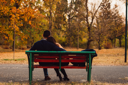 Boyfriend and girlfriend sitting on the bench together talking and kissing each other.