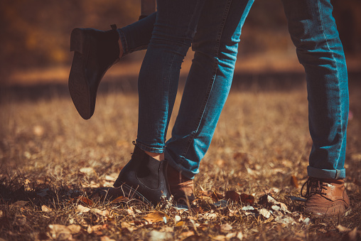 Sweet couple in jeans standing in the grass in the park, on the autumn leaves