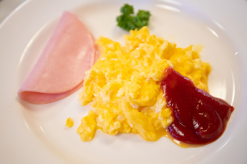 A top down view of simple scrambled eggs and ham with tomato sauce.
