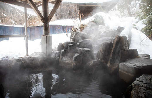 Japan is famous for hot spring baths. An outdoor hot spring bath with rock waterfall and snow around usually found at a Japanese Inn or Ryokan.