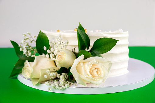 Wedding cake with white roses on green background. Close up.