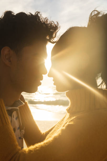 istock Back lit biracial couple face to face romancing at beach during sunset 1364704539