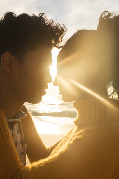 volta iluminada casal biracial cara a cara romancing na praia durante o pôr do sol - life back lit people happiness - fotografias e filmes do acervo