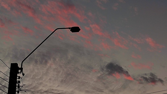 Silhouette unlit street light lamp during sunset. dark sky and pink cloud. city infrastructure.