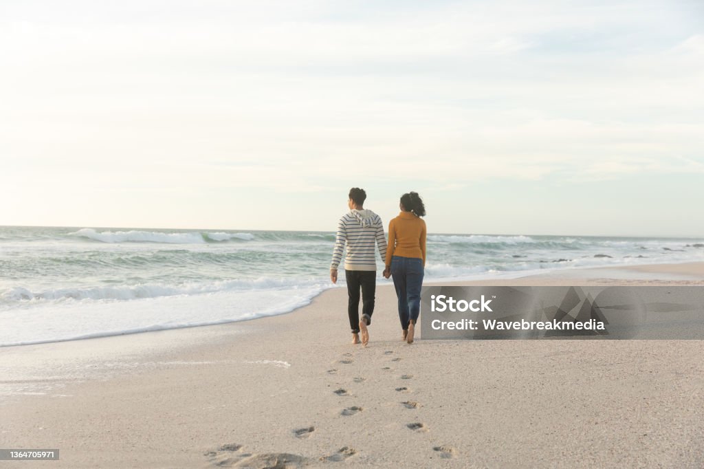 Full length rear view of biracial couple walking while leaving footprints on sand at beach Full length rear view of biracial couple walking while leaving footprints on sand at beach. lifestyle, love and weekend. Leaving Stock Photo