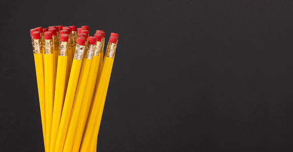 Leadership or financial graph concept: Yellow classic charcoal pencils with red eraser on black surface. Group of wooden objects pencil in row. One rising above the rest, representing progress and graph-like depiction. School, stationary, craft or office background with copy space. Set of 15 files