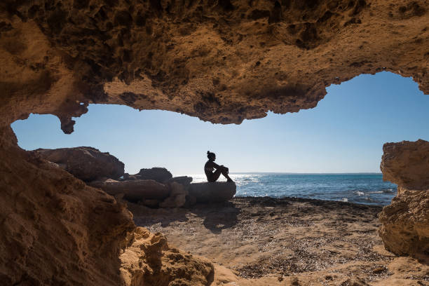 frau sitzt neben einer höhle in der nähe des meeres - insel formentera stock-fotos und bilder