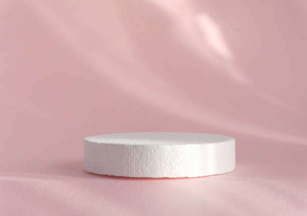 istock White round polystyrene showcase on abstract textured rose background, in rays of sunlight. 3D podium for demonstration of cosmetics 1364719284