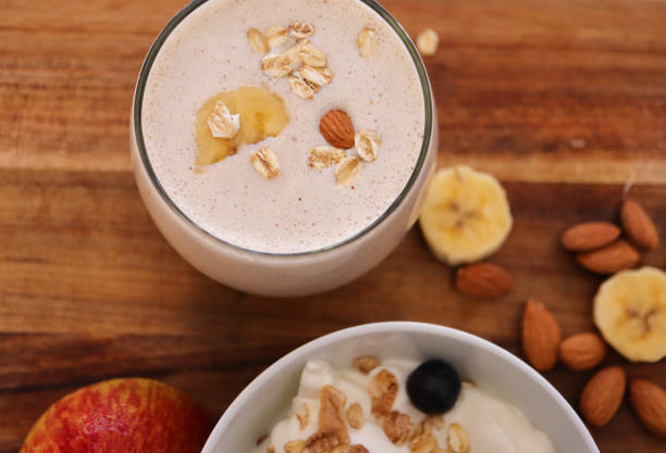 Apple and banana smoothie. Bowl of yogurt and muesli in foreground and almonds and sliced banana in background