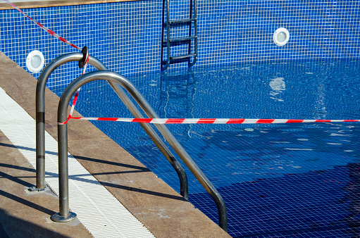 Red and white tape prohibits entry to swimming pool. Selective focus on pool with no-entry tape. Ban on visiting public places during the coronavirus epidemic.