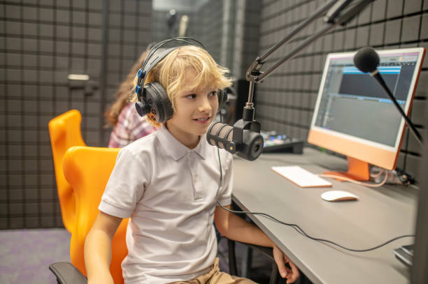 istock Pleased boy concentrated on recording a podcast in the studio 1364728648