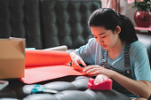 istock Asian young teenager girl making handmade items care package by cutting a red paper prepare to sending to her family or friends from distance. 1364729857