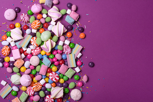Multicolored sweet and bright dragee, candies, lollipops, marshmallows for fun party on purple background