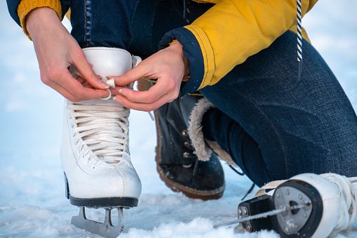 Young woman putting on ice skates. Female hands tying laces. Close up.