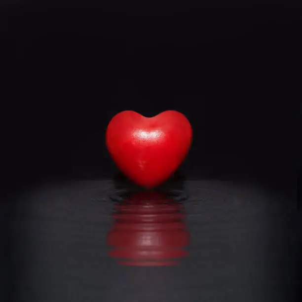 Photo of True love minimal concept. Red heart floating in black ripple water. Cool black background
