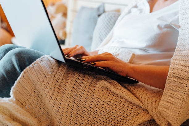 istock Remote work, home office, freelance concept. Side view of caucasian woman using on laptop while sitting on bed in bedroom, close-up. Selective focus on typing female hands browsing internet 1364735664