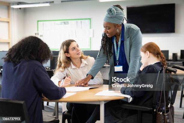 Female Students Working On Assignment With Help From Teacher Stock Photo - Download Image Now