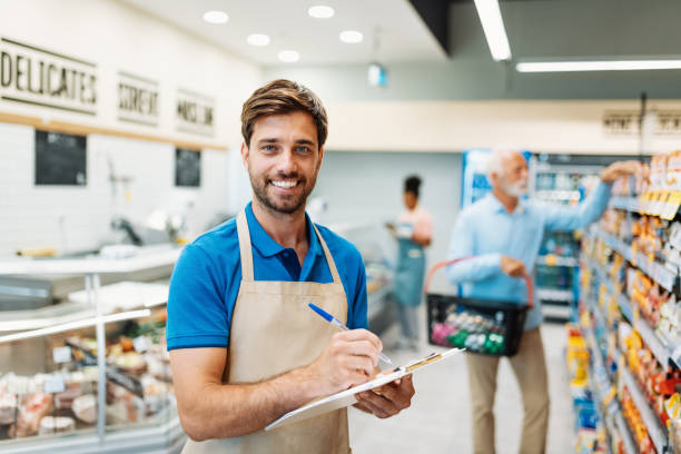 Employee in supermarket, store manager filling orders and smiling while looking at camera stock photo
