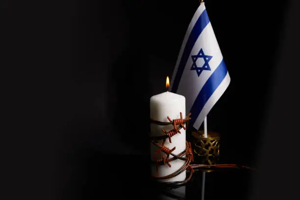 Barbed wire on burning candle and Israel flag on black background with space for text. Holocaust memory day.
