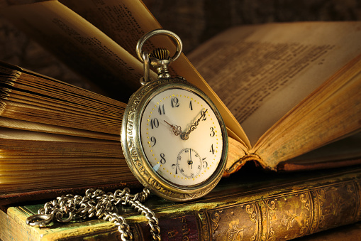 Vintage pocket watch with opened antique book. Old shabby wise books.