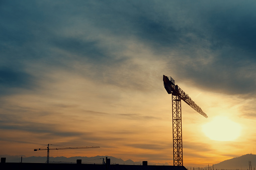 Cranes in silhouette on a housing development against a setting sun