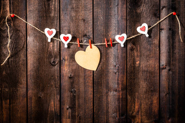 Valentines day background: cardboard heart hanging on a rope shot against weathered wood table. The composition is at the top of an horizontal frame leaving useful copy space for text and/or logo. High resolution 42Mp studio digital capture taken with Sony A7rII and Sony FE 90mm f2.8 macro G OSS lens