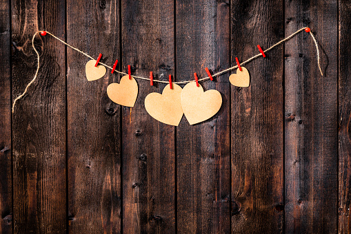 Valentines day background: several cardboard hearts hanging on a rope shot against weathered wood table. The composition is at the top of an horizontal frame leaving useful copy space for text and/or logo. High resolution 42Mp studio digital capture taken with Sony A7rII and Sony FE 90mm f2.8 macro G OSS lens