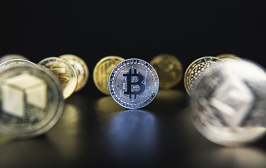 Silver Bitcoin next to many cryptocurrency coins like defocused Ethereum, Neo, Tether on black background. Central composition, low key photo for banners and news about BTC crypto.