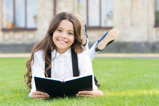 ihr hobby ist die literatur. glückliches kleines kind liest kinderliteratur im freien. entzückendes kleines mädchen genießt es, englische literatur in aller ruhe zu lesen. erlernen ausländischer literatur in der schule - childrens literature stock-fotos und bilder