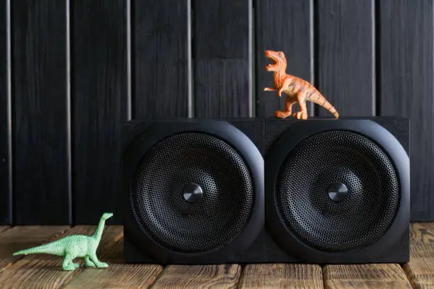 Two-way speaker system next to toy dinosaurs on a background of natural pine boards. An example of installing two-way acoustics in an environmentally friendly interior of a children's room. Close-up