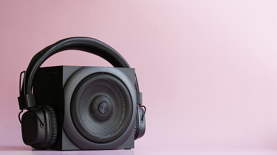Black audio speaker and headphones with ambryushores on a pink background. Pop music concept. Free space for text, inscription and labels. Close-up