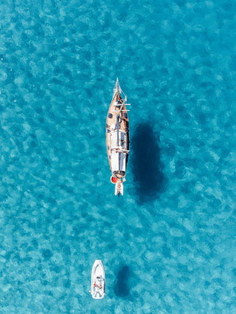 Aerial view of a sailboat and a speedboat against a clear turquoise sea's water Aerial view of a sailboat and a speedboat against a clear turquoise sea's water. Favignana Island se in Sicily, Italy. favignana photos stock pictures, royalty-free photos & images