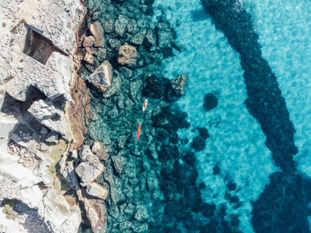 Beautiful turquoise water in Favignana Island, Sicily Beautiful turquoise water in Favignana Island, Sicily. High angle view of rocks in the sea. A woman is carrying her husband with a canoe while he's resting on a sup. egadi islands photos stock pictures, royalty-free photos & images