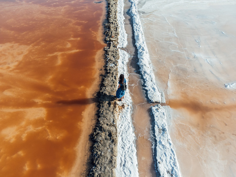 Aerial view of a woman standing in the middle of orange salt flats in Sicily, Italy. Trapani salt flats.