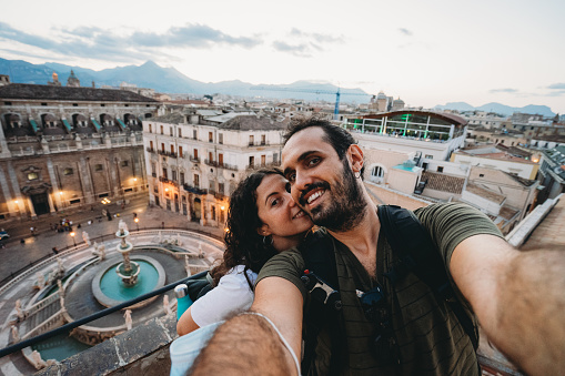 Millennial couple are taking a selfie in Piazza Pretoria, Palermo, Italy. Pov view.