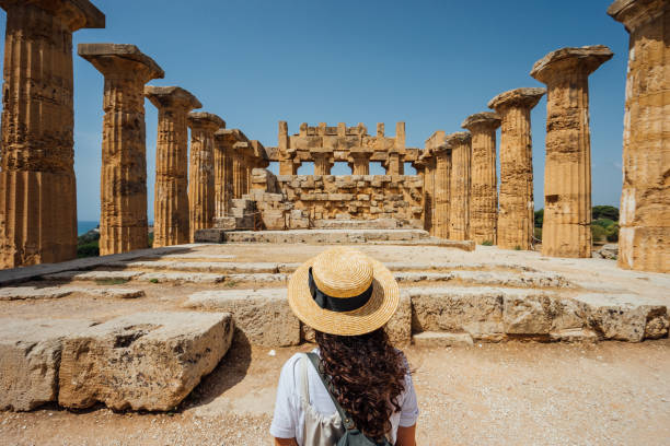 vista posteriore di una donna con un cappello mentre ammira un antico tempio in sicilia - archeologia foto e immagini stock