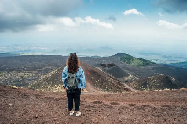 A woman is admiring a panoramic view of Mount Etna, an active volcano in Sicily, Italy. Black ground around the volcano.