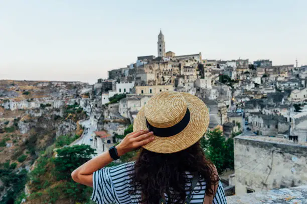 A woman with a straw hat is admiring the beautiful Matera ancient city. Sassi di Matera, a famous international landmark in Southern Italy.