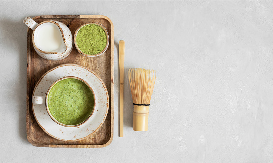 Matcha tea latte with milk, matcha powder in a wooden tray on a gray concrete background. Copy space, top view, flat lay.