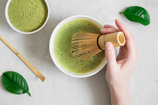 Matcha green tea. Woman hand brews matcha tea on a gray concrete background. Japanese tea ceremony. Top view, flat lay.