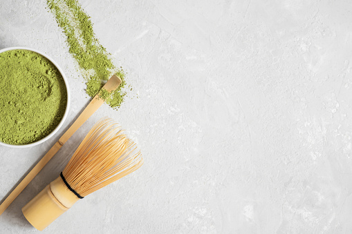 Matcha green tea powder, bamboo whisk and spoon on a gray background. Japanese drink. Tea ceremony. Copy space, top view, flat lay.