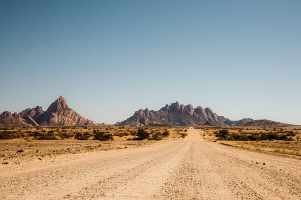 Driving the gravel road with scenic view of the Namibian landscape Panoramic view of the desert road with rocky landscape on the background in Spitzkoppe, Namibia dirt track stock pictures, royalty-free photos & images