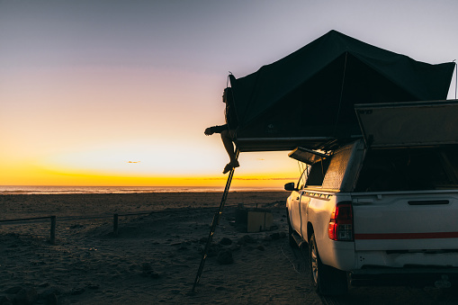 Female traveler admiring sunset at the Skeleton Coat, camping by the coastline with 4X4 camper truck, getting ready to sleep in the roof tent, Southern Africa