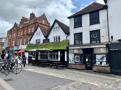 Street view of old town St Albans. An old English pub “The Boot” with tables outside. Facade decorated with baskets of geranium and ivy. Market place. Selective focus