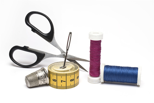 Sewing equipment like thread, needle, tape measure , zipper, scissors ,button, thimble and thread opener of blue fabric.