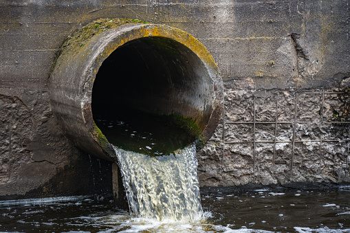 Dirty water flows from the pipe into the river, environmental pollution. Sewerage, treatment facilities.