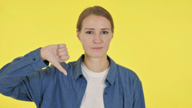 istock Thumbs Down Gesture by Young Woman on Yellow Background 1364760768